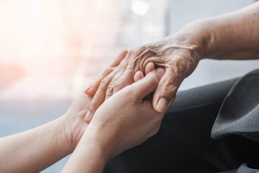 Close-up on the hands of a young family member holding the hand of a loved one in hospice care