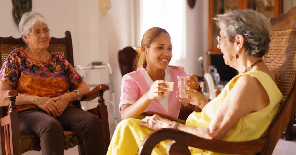 Hospice Nurse Serving Pill Medicine Water To Old Woman