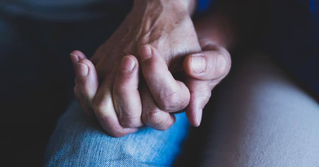 Close-up portrait of two hands of senior or mature people at home holding each other