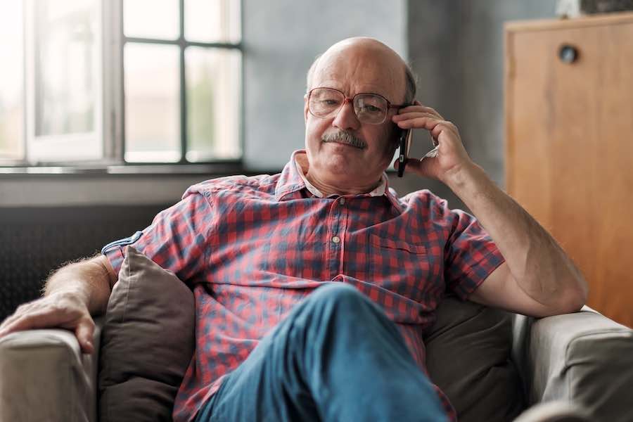 Retired-Hispanic-man-talking-on-phone-sitting-in-living-room.