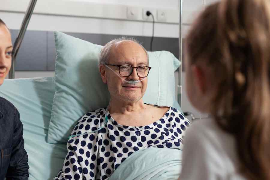 elderly sick old man resting in bed talking with caring granddaughter
