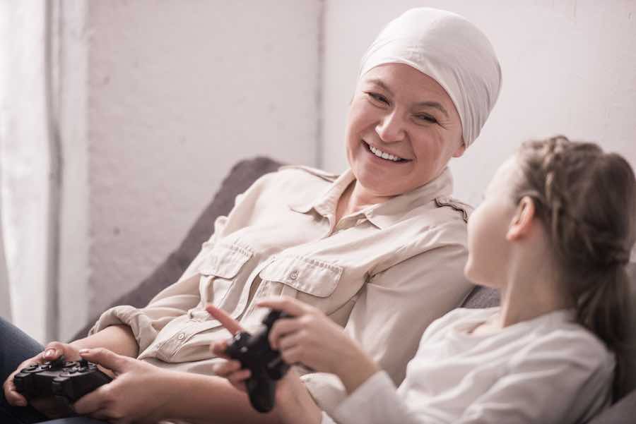 happy grandmother and granddaughter playing with joysticks, cancer concept
