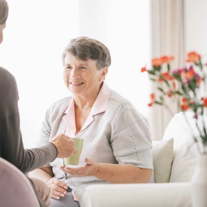 Caretaker handing beverage to elderly woman using integrative therapy services.