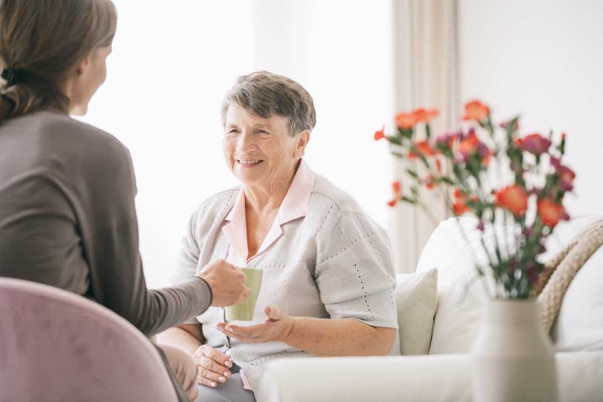 Caretaker handing beverage to elderly woman using integrative therapy services.