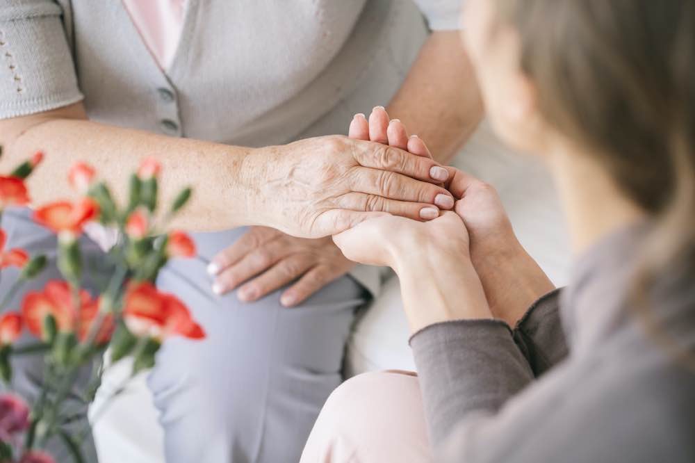 Caretaker holding hands of elderly woman receiving integrative therapy services.