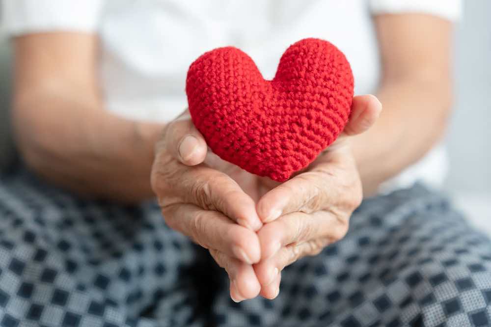 Senior woman holding a red yarn heart, symbolizing care in administering hospice medications.