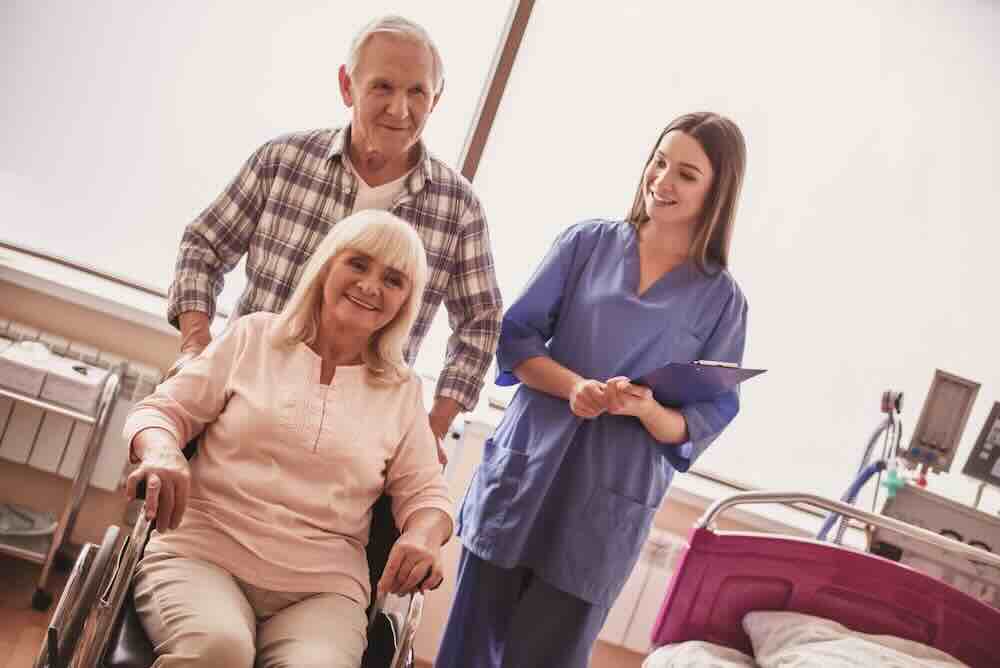 Old man pushing his wife in a wheelchair with an in home hospice caregiver.