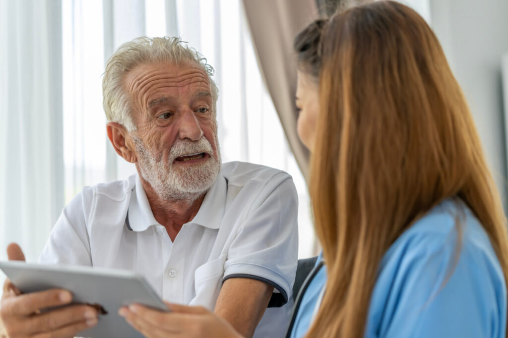 Elderly man talking with a nurse about who pays for hospice care.